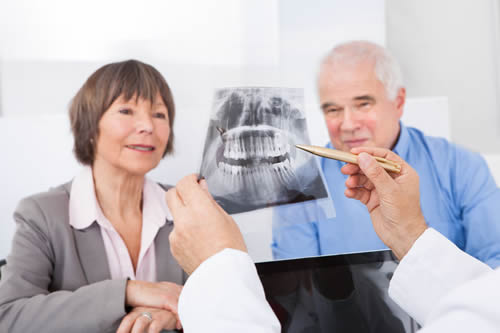 Male dentist explaining dental x-ray to senior couple in clinic.