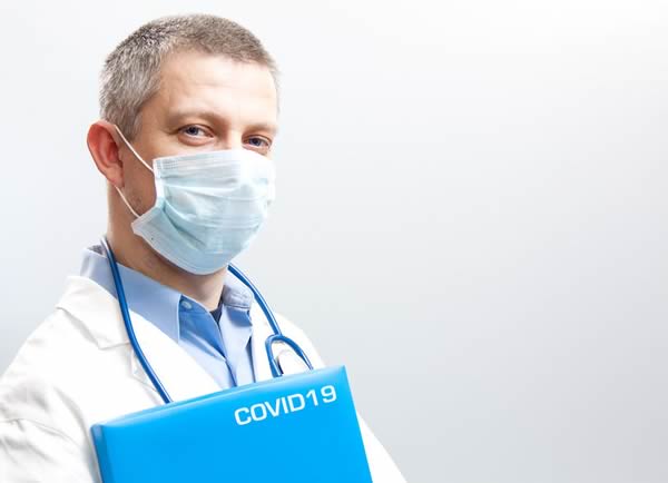 Dentist wearing face mask and holding folder that reads COVID-19.