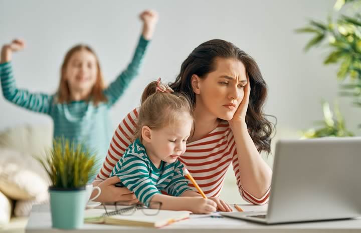 Woman working on a laptop at home and surrounded by children.