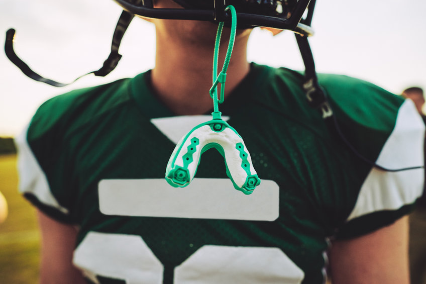 Closeup of a mouthguard hanging off the helmet of a young football player.